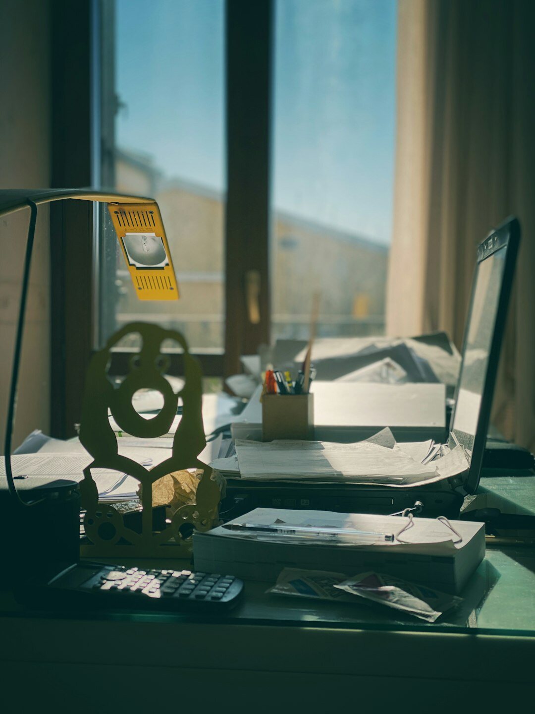 Desk covered with printed documents, a magnifying glass and a laptop